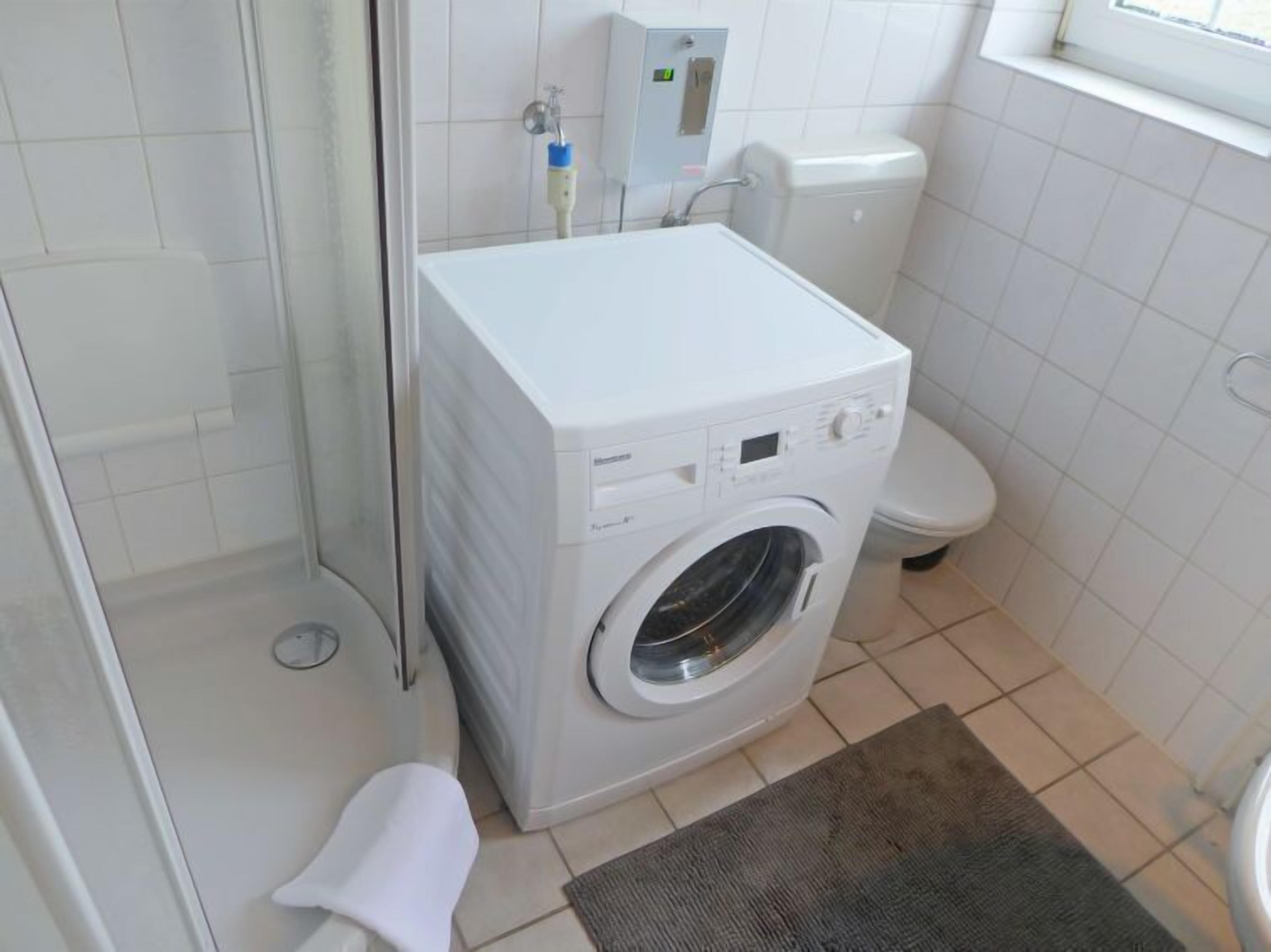 Een kleine badkamer met een wasmachine, toilet en een douchecabine van glas.