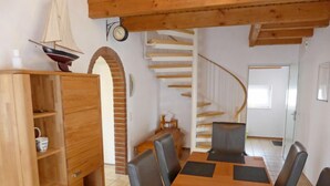 A dining area with a wooden table and chairs, a bookshelf, a clock, and a staircase. - Vacation home Reuse by Interhome (Norddeich)