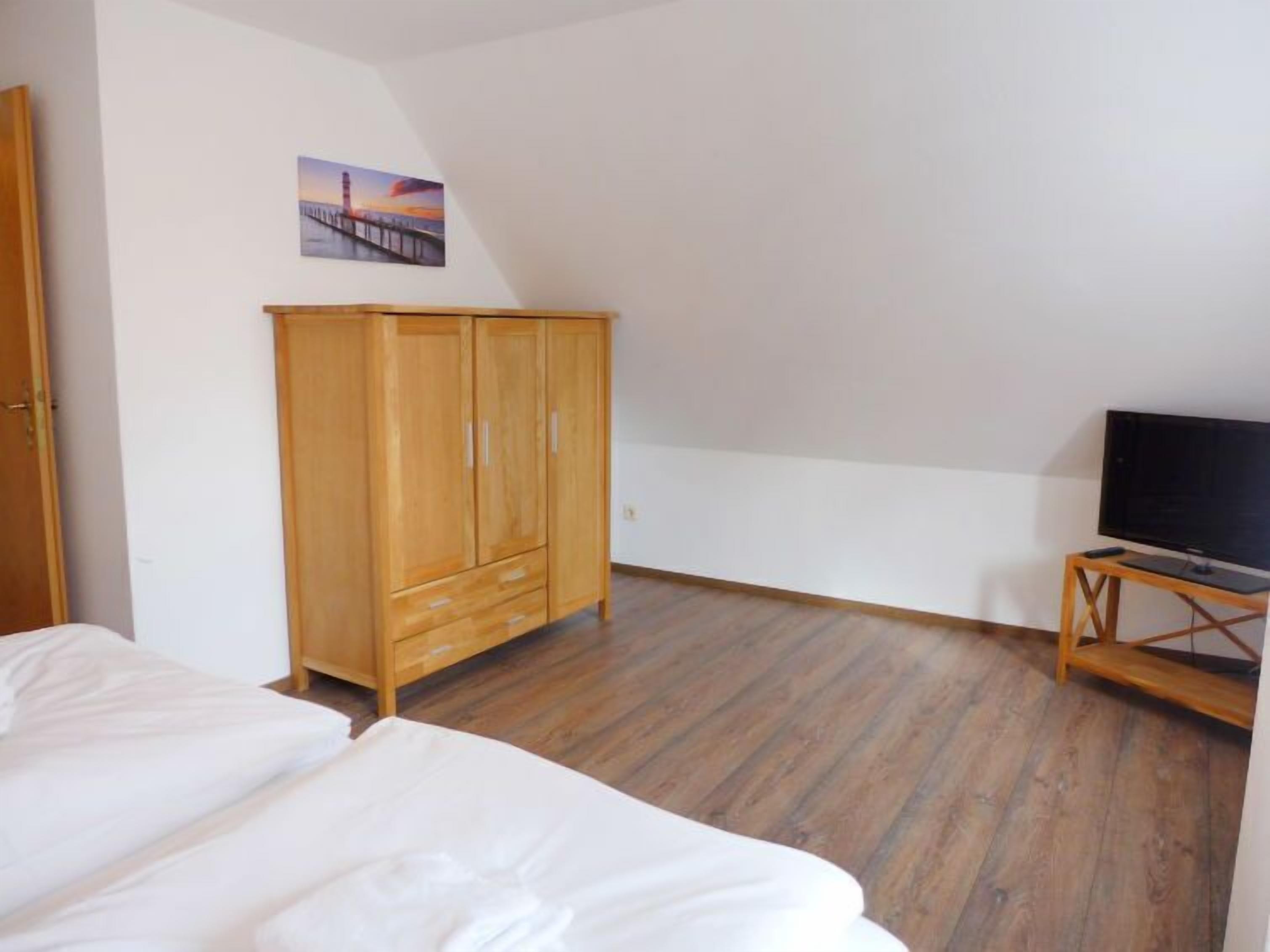 A bedroom with a bed, wooden wardrobe, television on a wooden stand, and a painting on the wall.