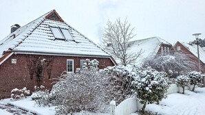 A snow-covered residential area with brick houses, a white picket fence, and snow-laden bushes. - Vacation home Reuse by Interhome (Norddeich)