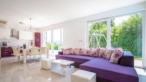 Een moderne woonkamer met een paarse bank, een witte salontafel en een eethoek met een tafel en stoelen.