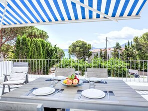 An outdoor dining area with a table set for two, a view of the sea, and a blue and white striped awning.