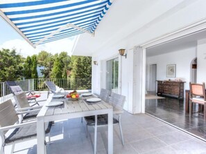 A balcony with a table set for dining, chairs, and a blue-striped awning.