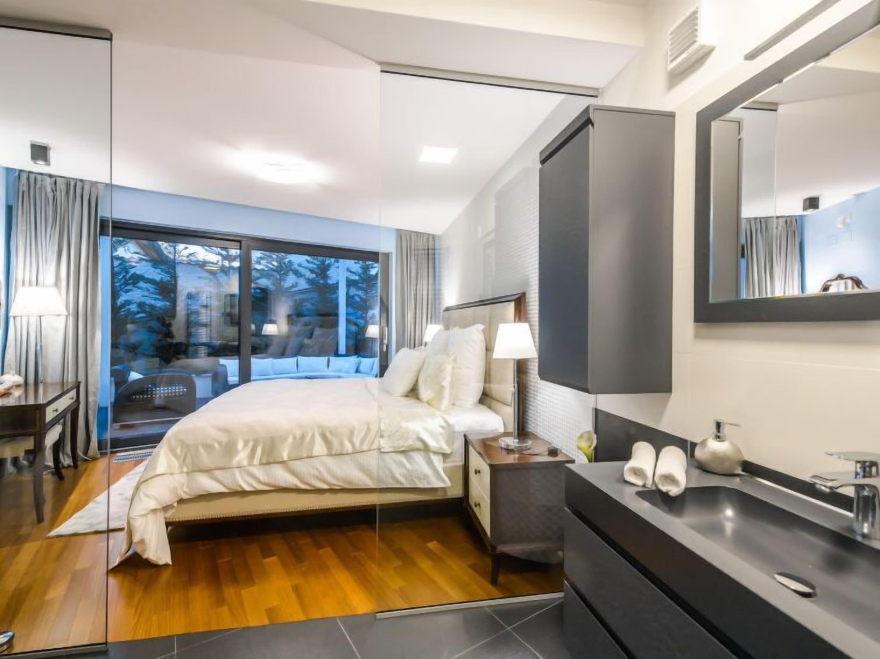 A modern hotel room with a large bed, a bathroom with a black sink and mirror, and a view of trees through the window.