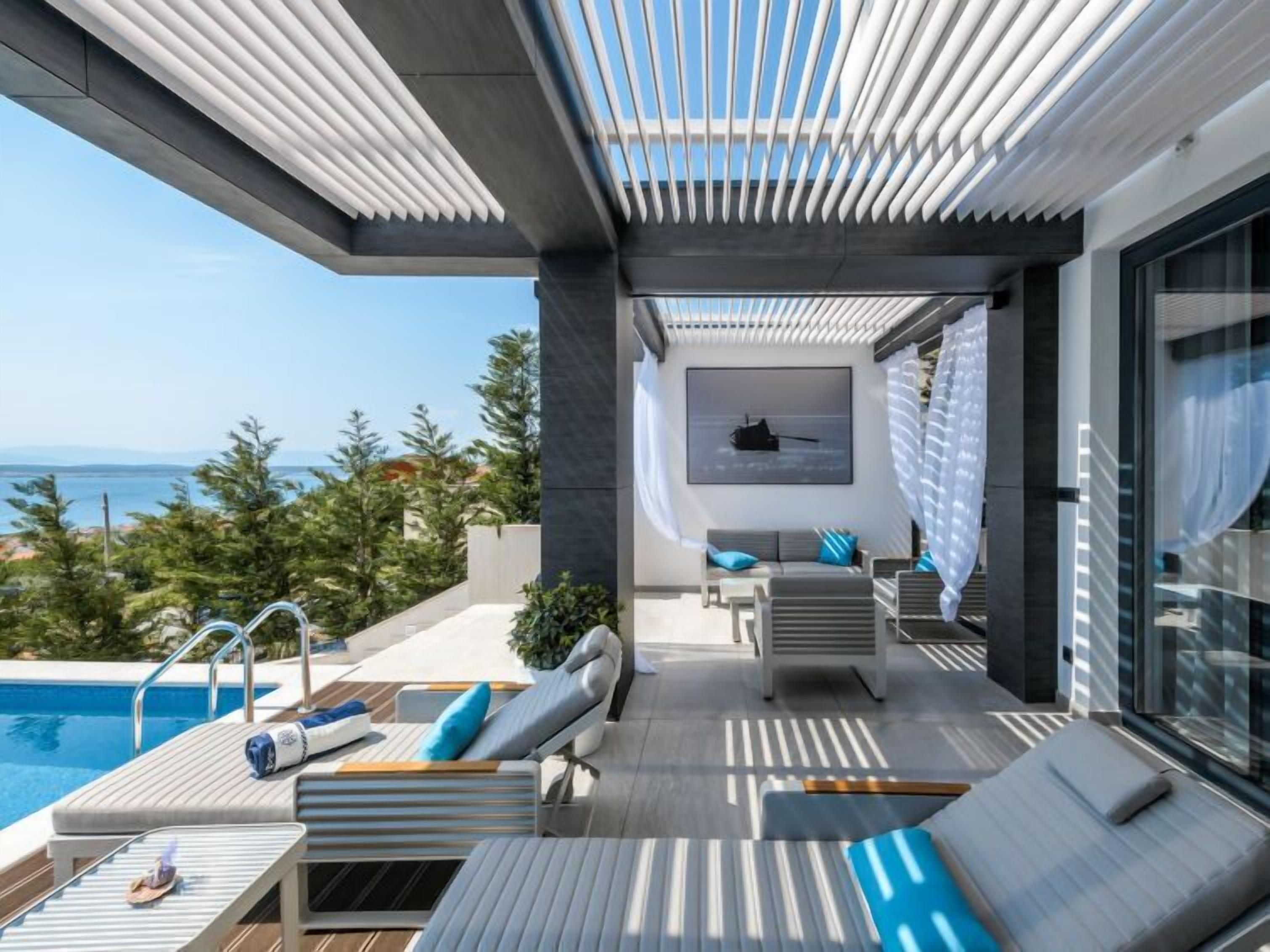 Een modern terras buiten met een zwembad, ligbedden en uitzicht op zee.