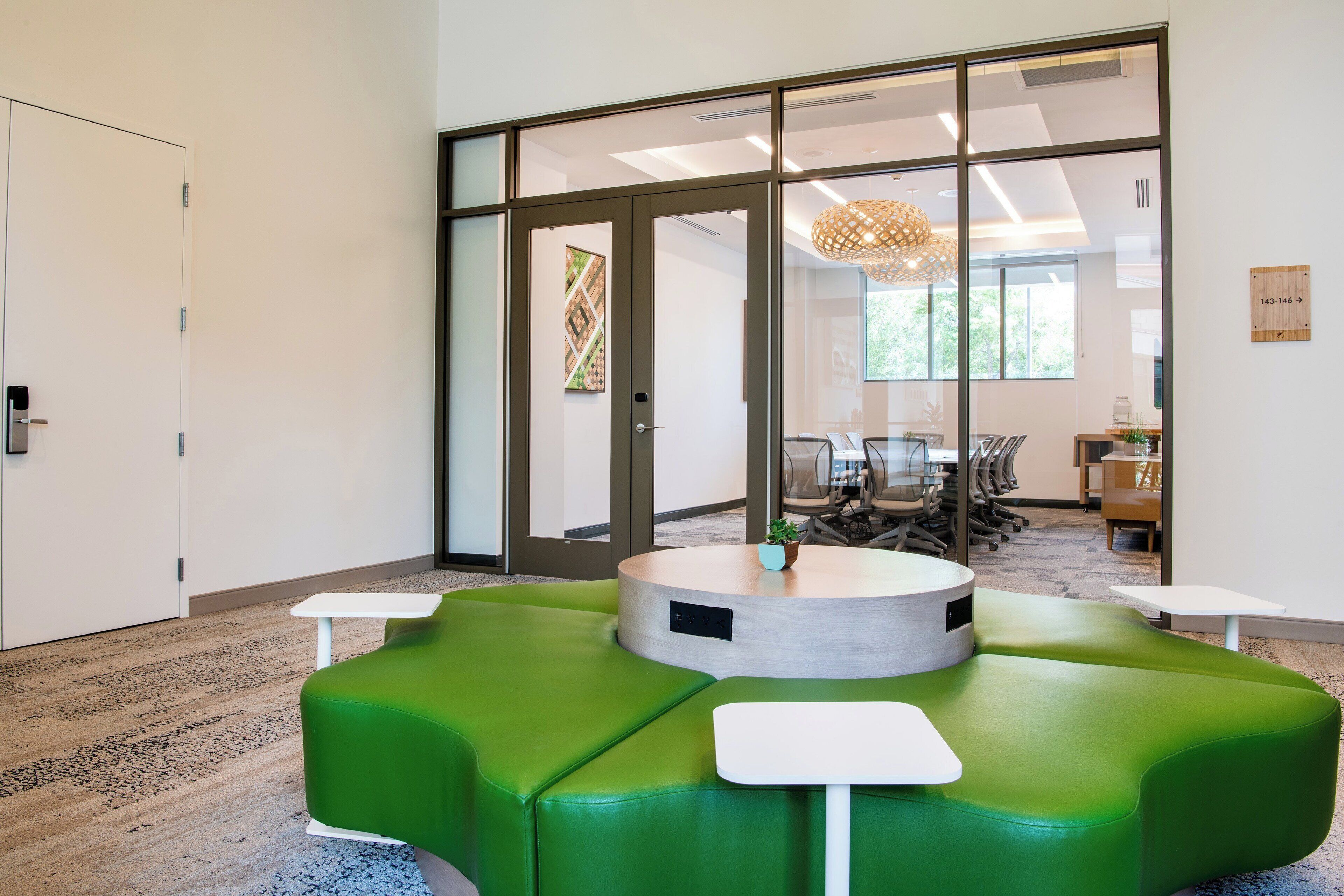 A modern office space with a green seating area, a round table, and a glass door leading to a conference room.