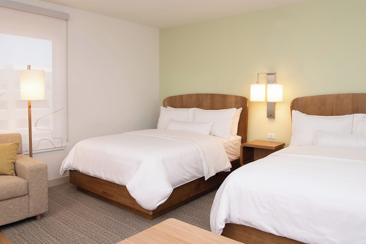 A hotel room with two beds, a sofa, and a lamp.