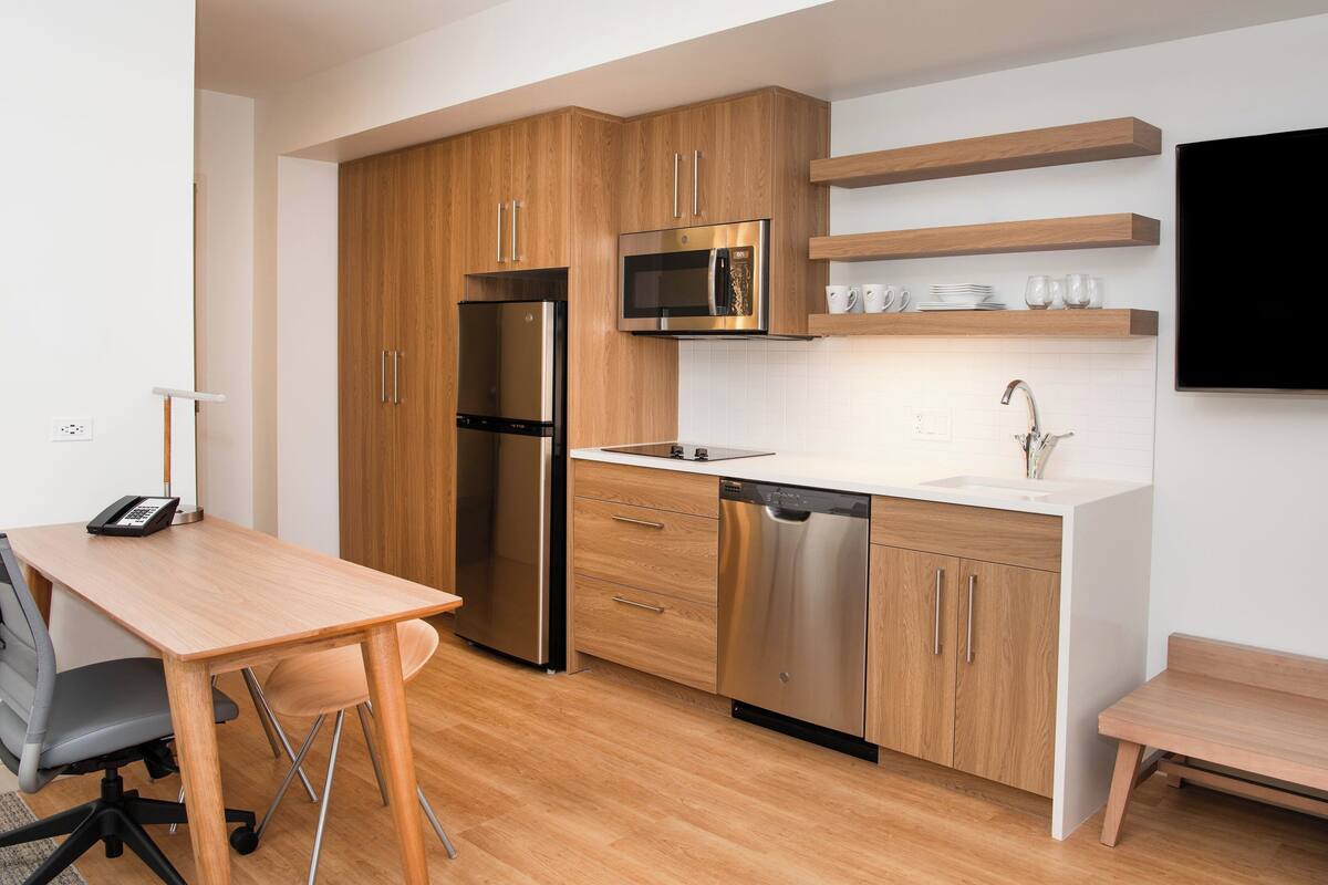 A modern kitchen with wooden cabinets, stainless steel appliances, a built-in microwave, and a flat-screen TV.