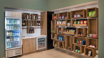 Um refrigerador abastecido com diversas bebidas, um compartimento refrigerado e prateleiras com lanches e produtos embalados.