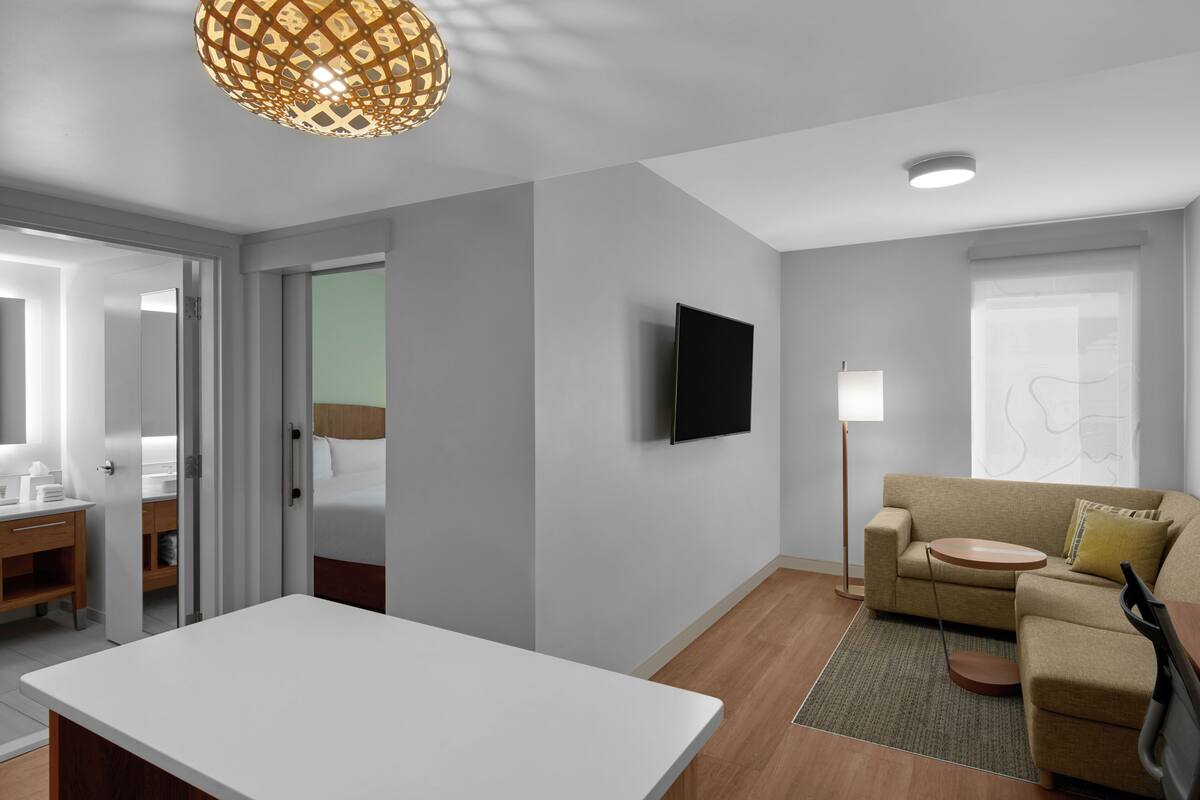 A modern hotel room with a flat-screen TV, a sofa, a small round table, and a dining table.