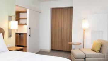 A hotel room with a bed, a sofa, a wooden wardrobe, a small round table, and a lamp.