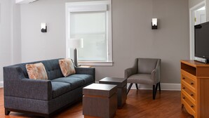 Ein Wohnzimmer mit grauem Sofa, grauem Sessel, einem Holz-TV-Schrank und einem kleinen Tisch.