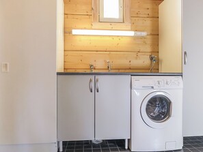 A compact laundry room with a washing machine, wooden cabinets, and a small window.