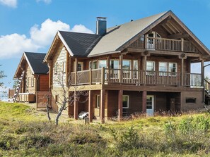 Een houten chalet met twee verdiepingen, een balkon, schoorsteen en een terras.
