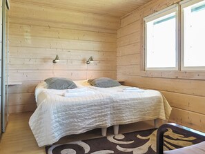 Een eenpersoonsbed met een witte sprei, twee bedlampjes en een raam met jaloezieën.