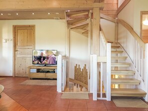 Een woonkamer met een houten trap, een televisie en een deur.