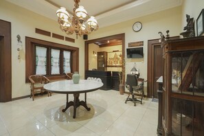 A dining area with a round table, chairs, a chandelier, and a clock on the wall. - OYO 804 Ndalem Maharani Guest House (Yogyakarta)
