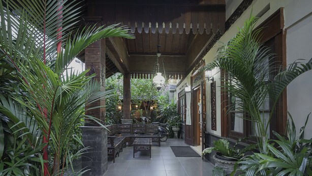 A covered outdoor seating area with benches and potted plants. - OYO 804 Ndalem Maharani Guest House (Yogyakarta)