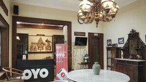 A hotel lobby with a reception desk, a chandelier, a round marble table, and a large clock on the wall. - OYO 804 Ndalem Maharani Guest House (Yogyakarta)