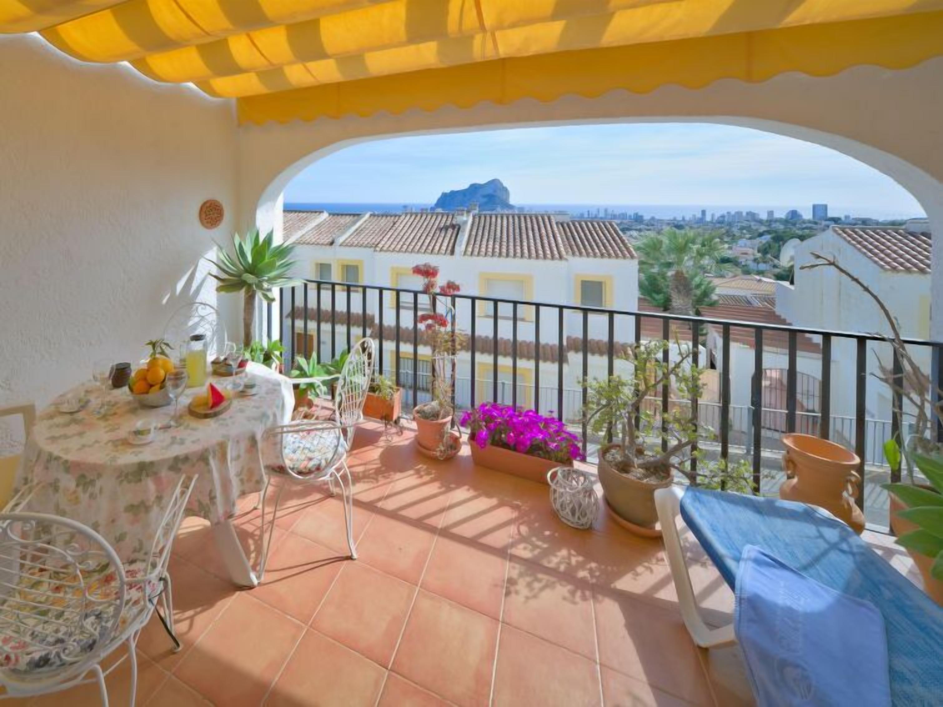 A balcony with a table set for a meal, potted plants, and a view of the cityscape.