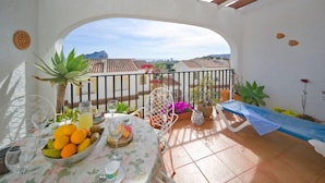 Een balkon met een ontbijtsetje, uitzicht op de stad en een pergola erboven.