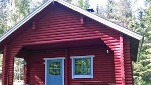 A red log cabin with a porch, a door, and two windows.