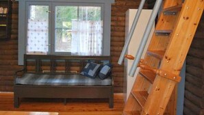 A wooden cabin interior with a bench, a ladder, and a window overlooking a yard.