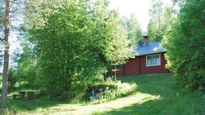 A red cabin with a blue roof surrounded by dense green trees.