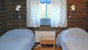 A room with two beds, a window with curtains, a heater, and a small wooden table.