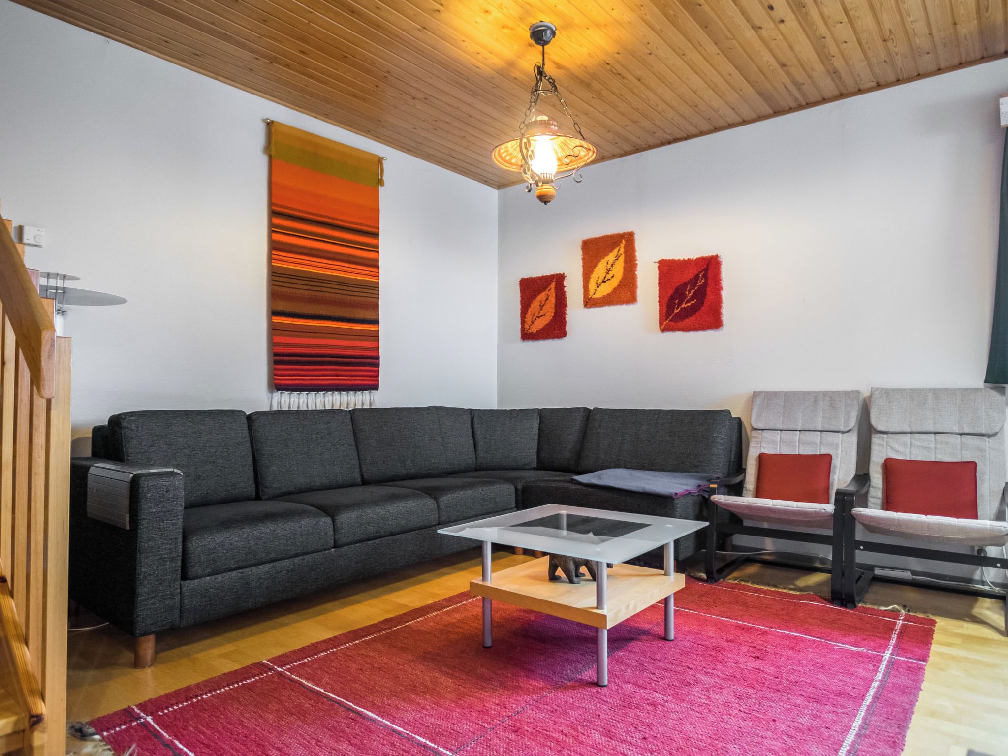 Una sala moderna con un sofá modular, una mesa de centro de vidrio y una alfombra roja.