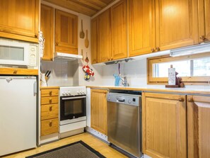 Une cuisine avec des meubles en bois, un four à micro-ondes, un four traditionnel, un lave-vaisselle et une fenêtre.
