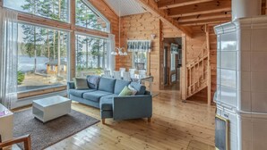 Un vaste espace de vie avec un intérieur en bois, de grandes fenêtres, un canapé et une cheminée.