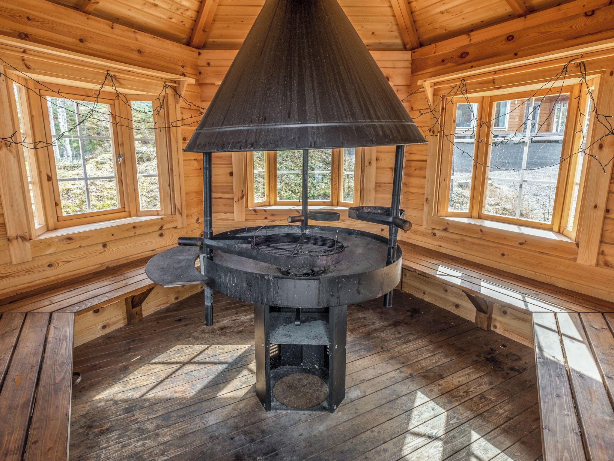 A wood-paneled room with a central wood-burning stove, large windows, and a sloped ceiling.