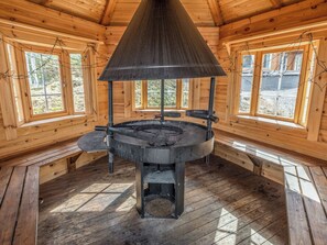 A wood-paneled room with a central wood-burning stove, large windows, and a sloped ceiling.