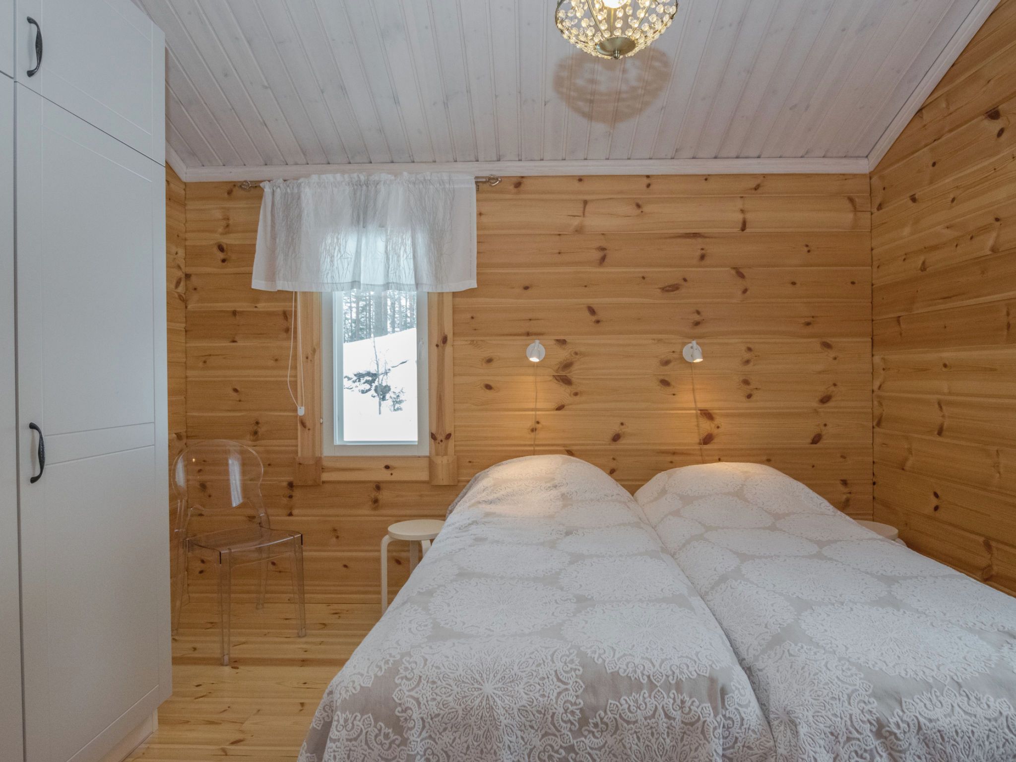 A wooden cabin room with a bed, a window, and a wardrobe.