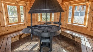 Une cabane en bois dotée d’un poêle à bois central, de grandes fenêtres et d’un plafond en pente.