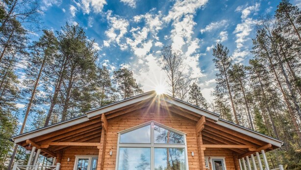 Une cabane en bois dotée d’une grande fenêtre en verre, d’un porche et offrant une vue sur la forêt environnante.