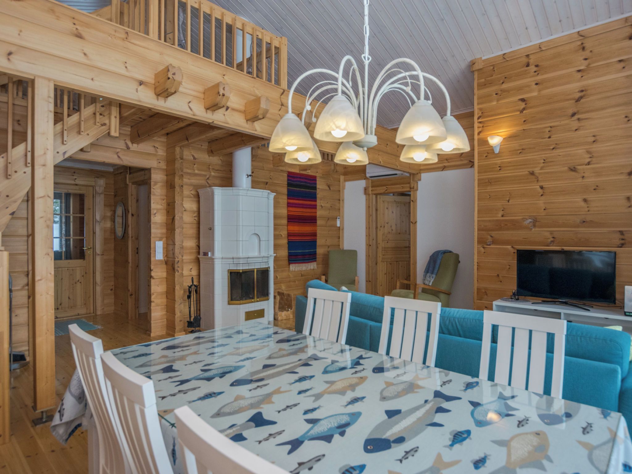 A wooden interior with a dining table, chairs, a television, and a fireplace.