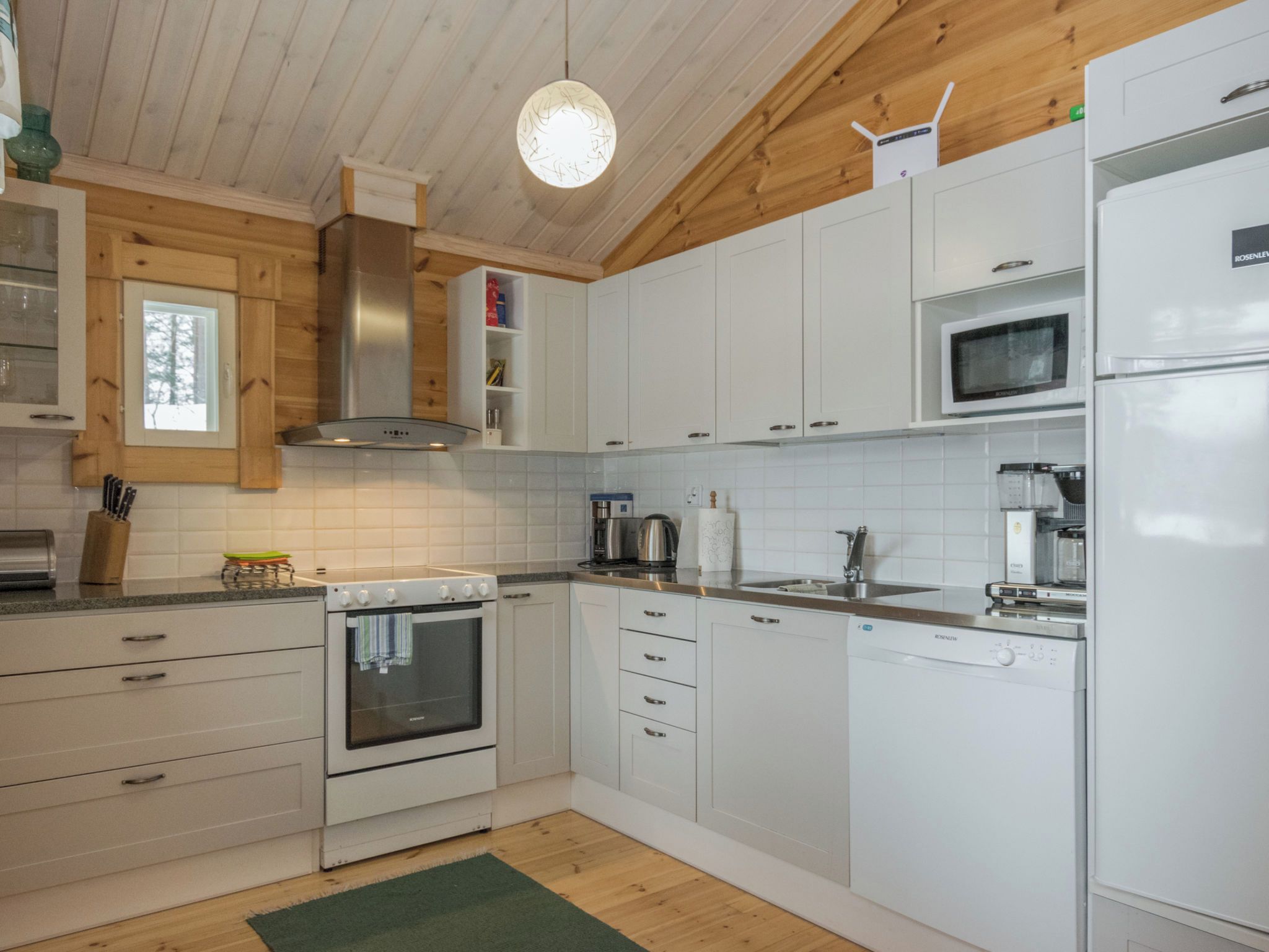 A modern kitchen with white cabinets, stainless steel appliances, and a wooden ceiling.
