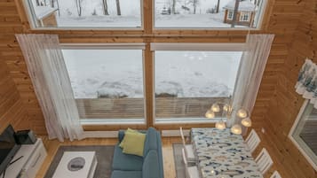 Interior acogedor de una cabaña con un ventanal grande, un sofá, una mesa y un comedor.