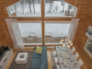 A cozy cabin interior with a large window, a sofa, a table, and a dining area. - Ritalahti by Interhome (Mäntyharju)