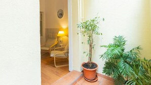Una habitación pequeña y acogedora con suelo de madera, una sola silla, una mesa con lámpara y una planta en maceta.