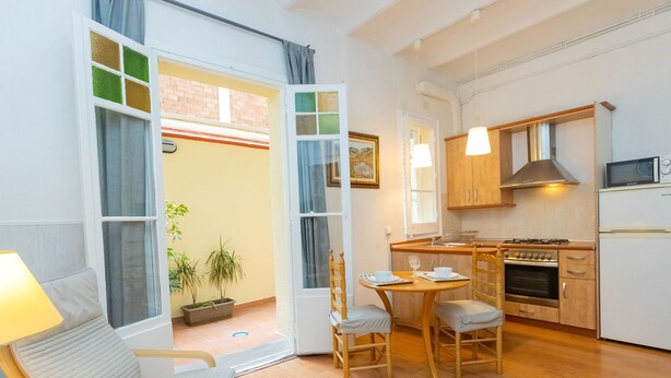 Una cocina acogedora con armarios de madera, una estufa y un microondas. Hay una zona de comedor con una mesa y sillas, y una ventana con cortinas.