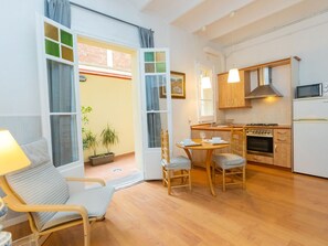 A cozy kitchen with wooden cabinets, a stove, and a microwave. There is a dining area with a table and chairs, and a window with curtains. - Gracia Torrijos by Interhome (Barcelona)