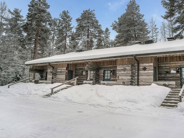 A log cabin with a snow-covered roof, wooden exterior, and a staircase leading to the entrance.
