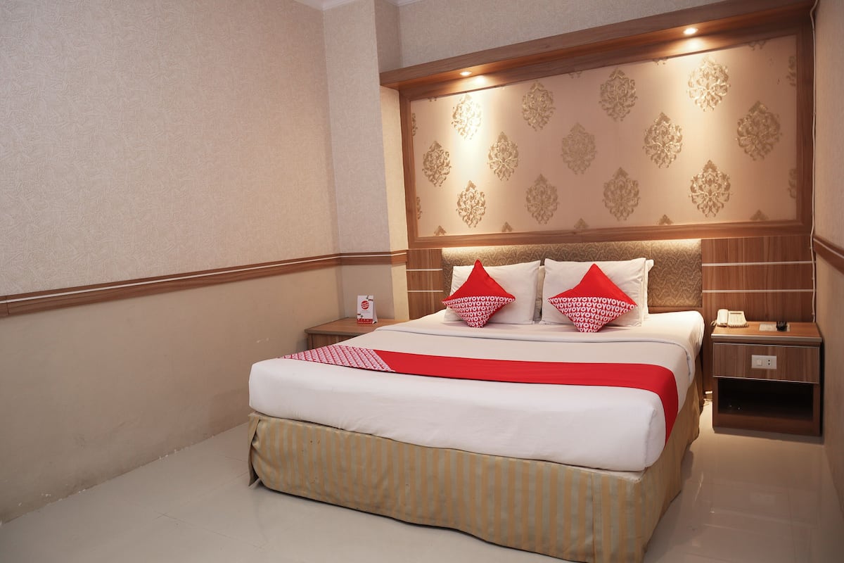 A hotel room with a large bed, a wooden headboard, a bedside table, and a nightstand.
