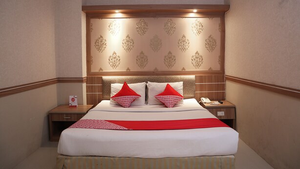 Ein Hotelzimmer mit einem großen Bett, zwei Nachttischen, einem Holz-Kopfteil und einer roten Tagesdecke.