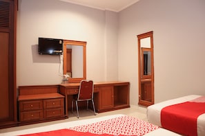 A hotel room with a wooden desk, a chair, a television mounted on the wall, a large mirror, and a bed with red bedding. - OYO 742 Mona Plaza Hotel (Pekanbaru)