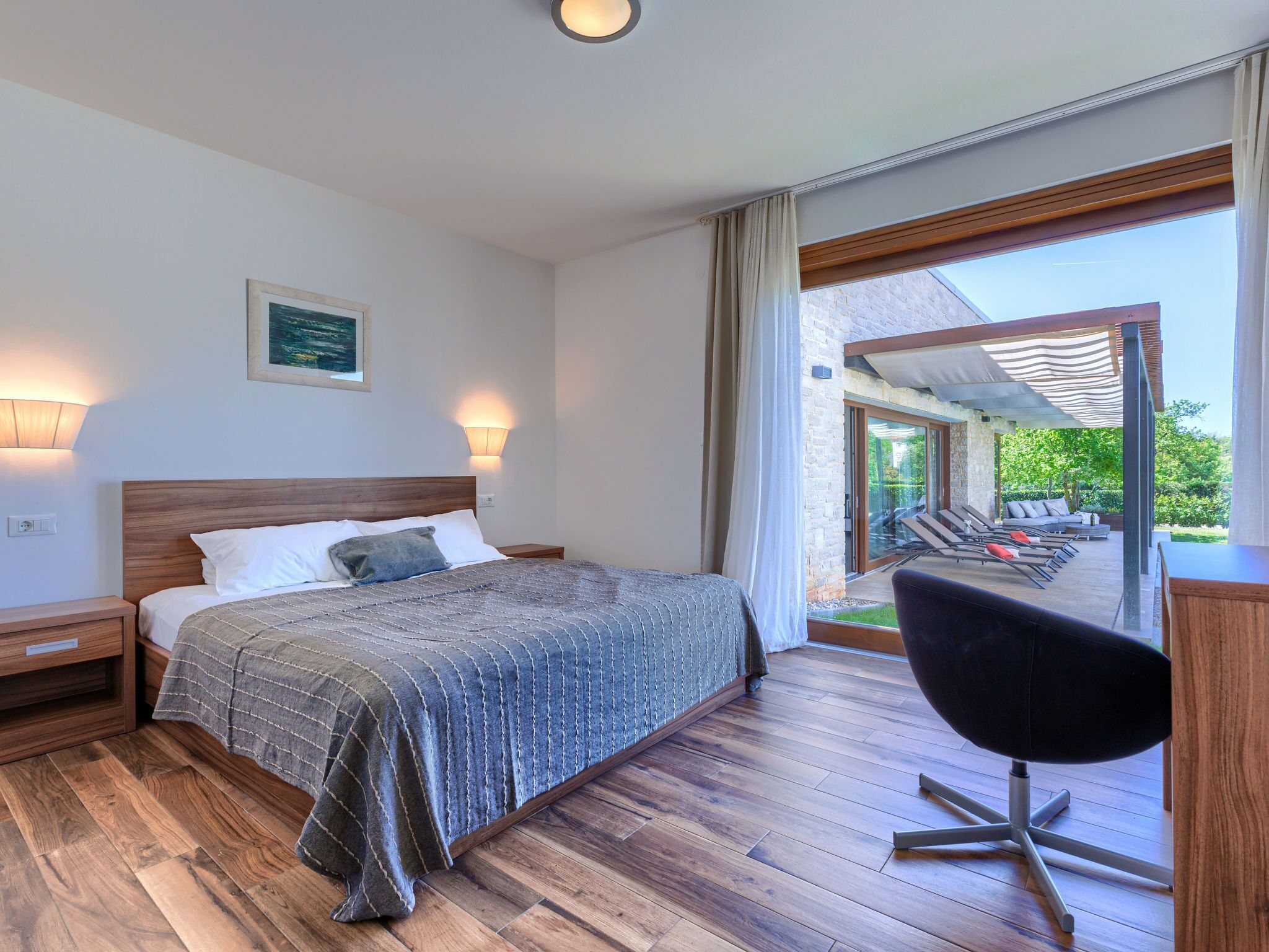 A bedroom with a large bed, a desk, and a view of the outdoors.