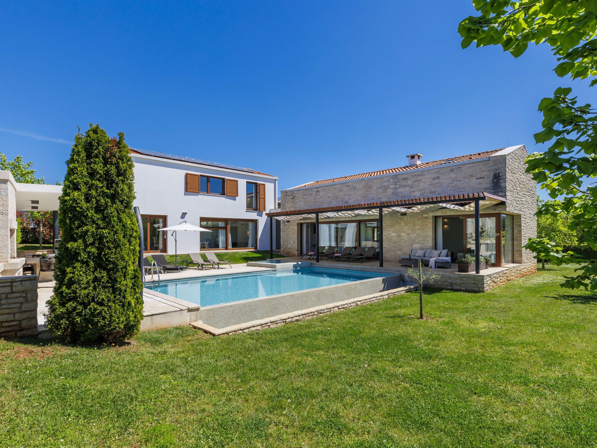 A modern house with a swimming pool, a covered patio, and a well-maintained lawn.